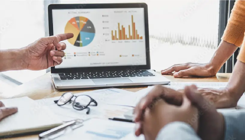 グラフが表示されたPCを囲んで会議をしている様子